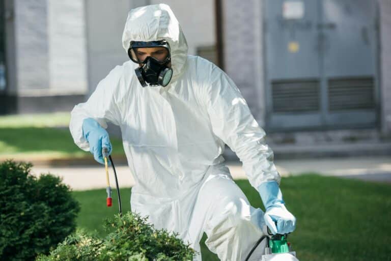 male pest control worker in uniform spraying chemicals on bush