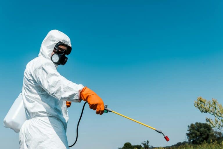 exterminator in protective uniform holding toxic spray outside