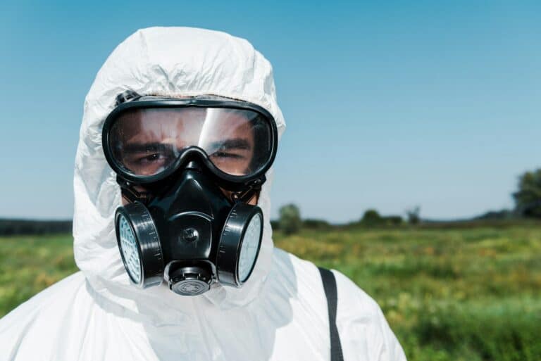 exterminator in uniform and protective mask looking at camera against sky