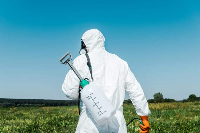 exterminator in white uniform with toxic spray outside